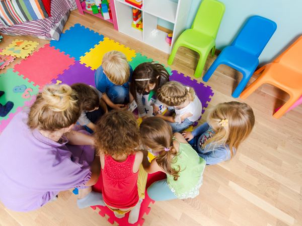 Eine Gruppe von Kindern sitzt in einem farbenfrohen Raum auf bunten Matten zusammen und beschäftigt sich mit einem gemeinsamen Spiel oder Aktivität.