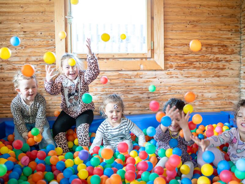 Fünf kleine Kinder toben lachend in einem Bällebad.