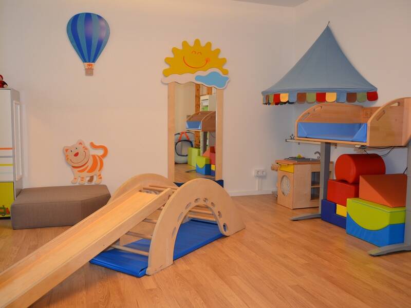 In einem Spielzimmer stehen eine kleine Rutsche aus Holz und bunte Bauklötze aus Schaumstoff.