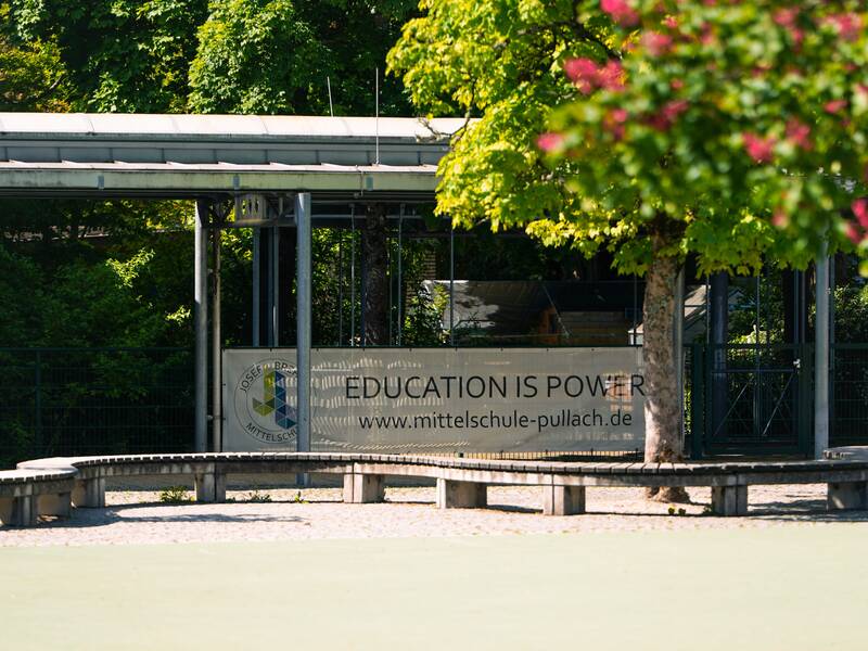 Auf einem Schulhof steht ein blühender Baum. Im Hintergrund hängt ein Banner mit der Aufschrift: Education is Power.