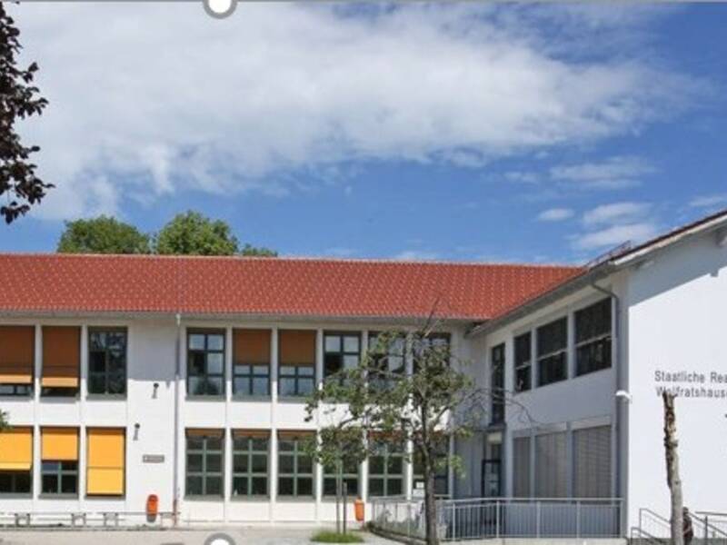 Ein großes weißes Schulhaus mit rotem Dach und gelben Jalousien.