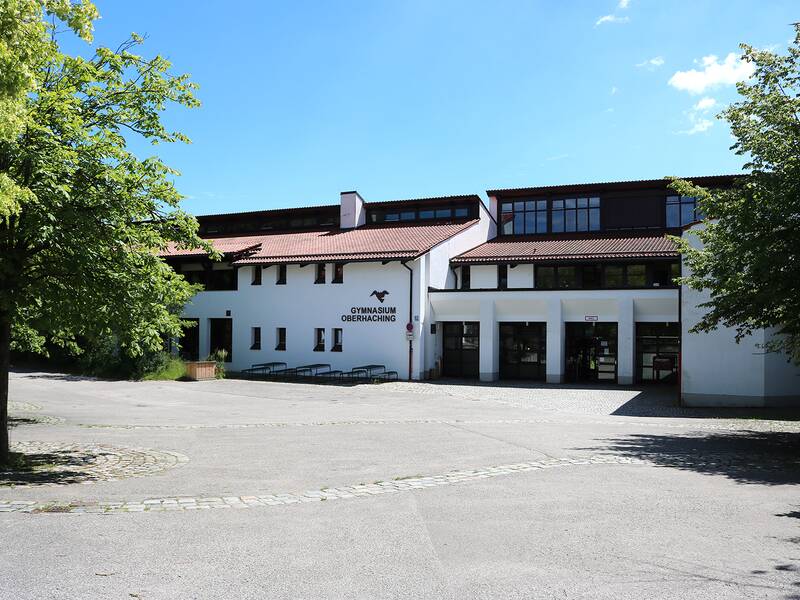 Vor einem weißen Schulgebäude erstreckt sich ein großer einladender Pausenhof.