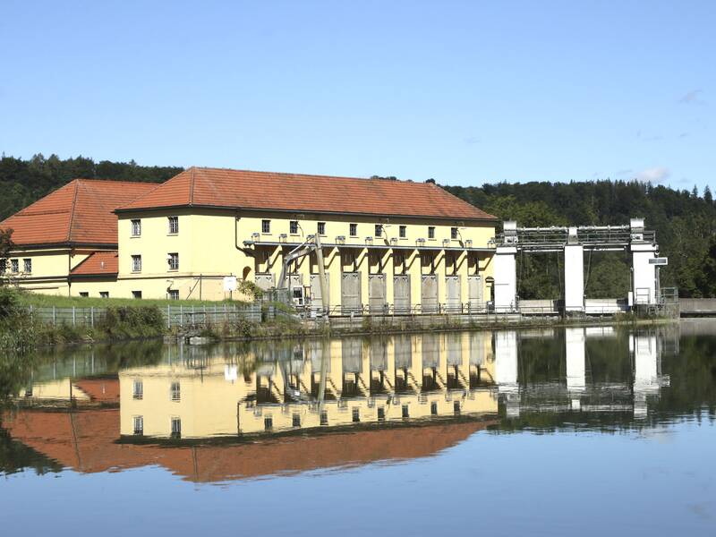 Eine gelbes Wasserkraftwerk spiegelt sich im Wasser des Isarkanals-