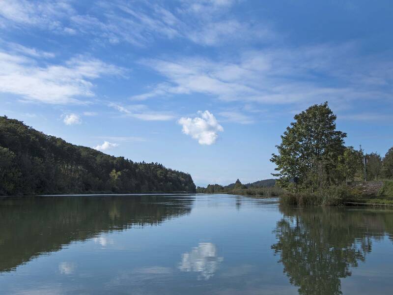 In einem ruhigen Flusß spiegeln sich Bäume und Wolken.