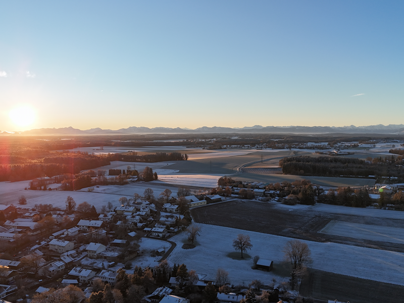 Drohnenbild mit Blick in die Berge, Gemeinde Straßlach zur Winterzeit mit Schneebedeckten Häusern und Feldern 