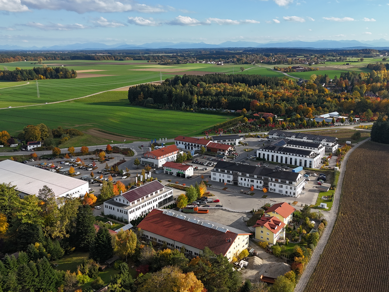 Eine Luftaufnahme zeigt einen Gewerbepark mit mehreren Gebäuden und Parkplätzen, umgeben von Straßen und landwirtschaftlichen Feldern.