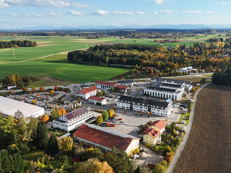 Eine Luftaufnahme zeigt einen Gewerbepark mit mehreren Gebäuden und Parkplätzen, umgeben von Straßen und landwirtschaftlichen Feldern.