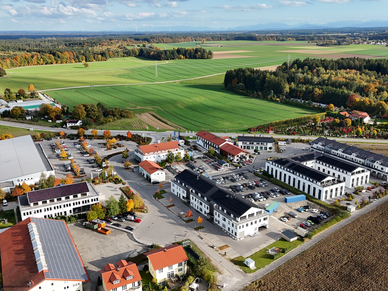 Eine Luftaufnahme zeigt einen Gewerbepark mit mehreren Gebäuden und Parkplätzen, umgeben von Straßen und landwirtschaftlichen Feldern.