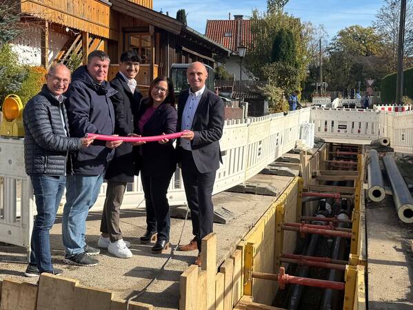 Fünf Menschen stehen an einer Straßenbaustelle und halten ein magentafarbenes Kabel.
