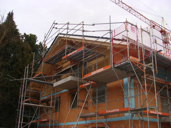 Der Rohbau eines Hauses ist eingerüstet. Blick auf die Giebelseite. 