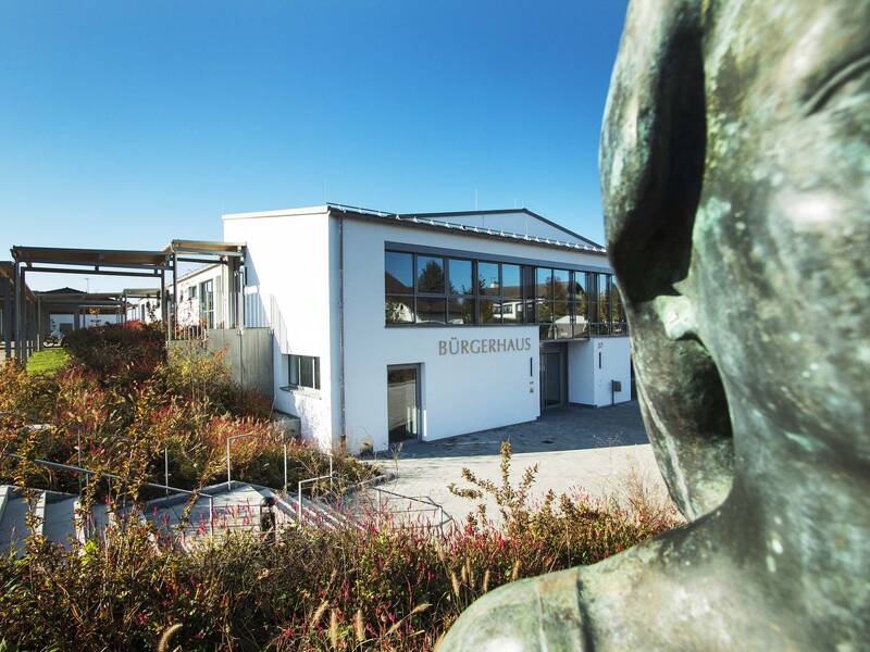 Hinter einer Bronzestatue befindet sich ein großes weißes Gebäude mit der Aufschrift Bürgerhaus. 