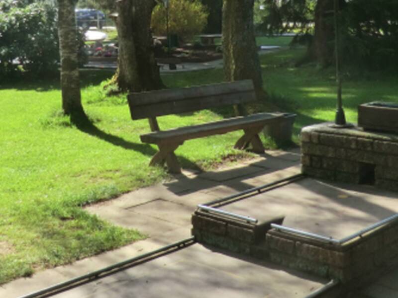 Neben einer Minigolfbahn steht eine Parkbank.
